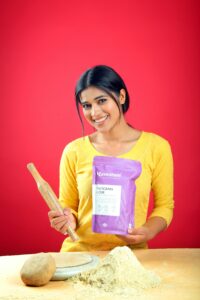 A woman holds a rolling pin and flour in a vibrant studio setting, ready to bake.